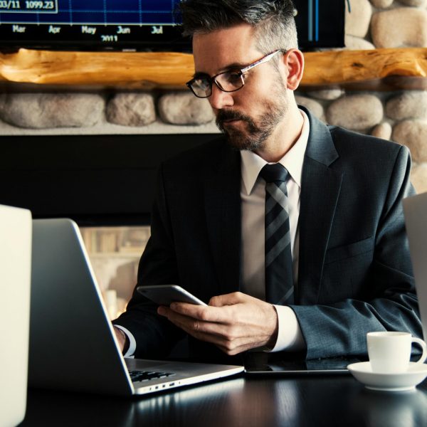 pexels-photo-618613-618613 Businessman in formal attire working on a laptop and smartphone at an indoor office desk.
